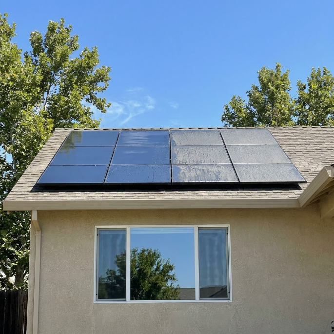 Solar panels on a house roof above a window under a blue sky.
