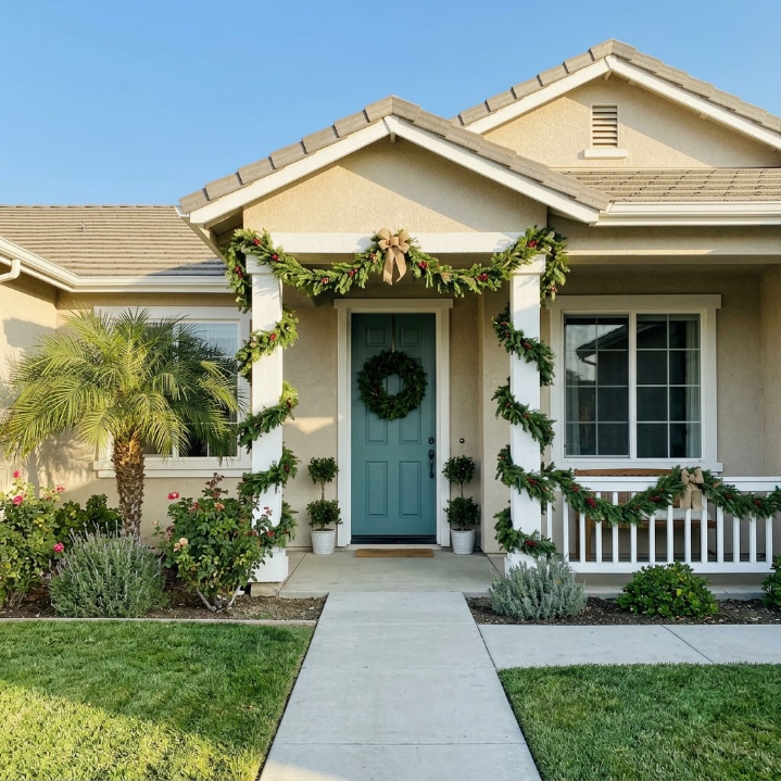 Suburban house with a blue front door, white porch railing, and greenery along the walkway