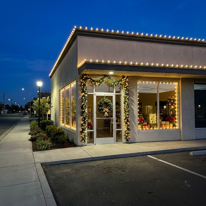 Corner storefront at dusk with warm holiday lights and decorated windows, viewed from the parking lot
