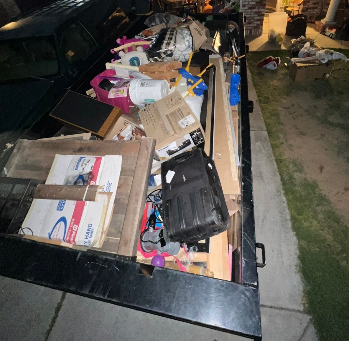Packed truck bed filled with boxes, tools, and clutter, parked beside a grassy area at night