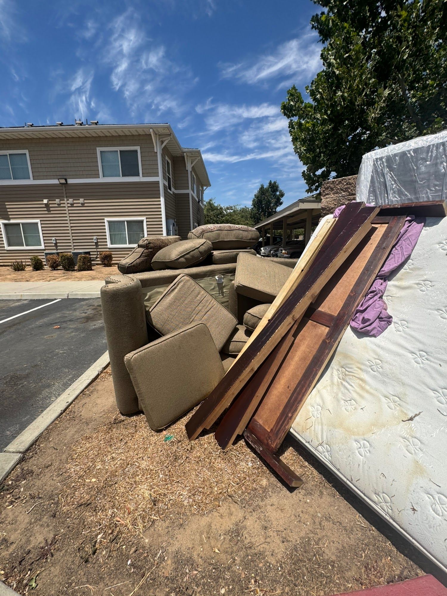 Furniture and lumber piled beside a roadside dumpster in front of apartment buildings