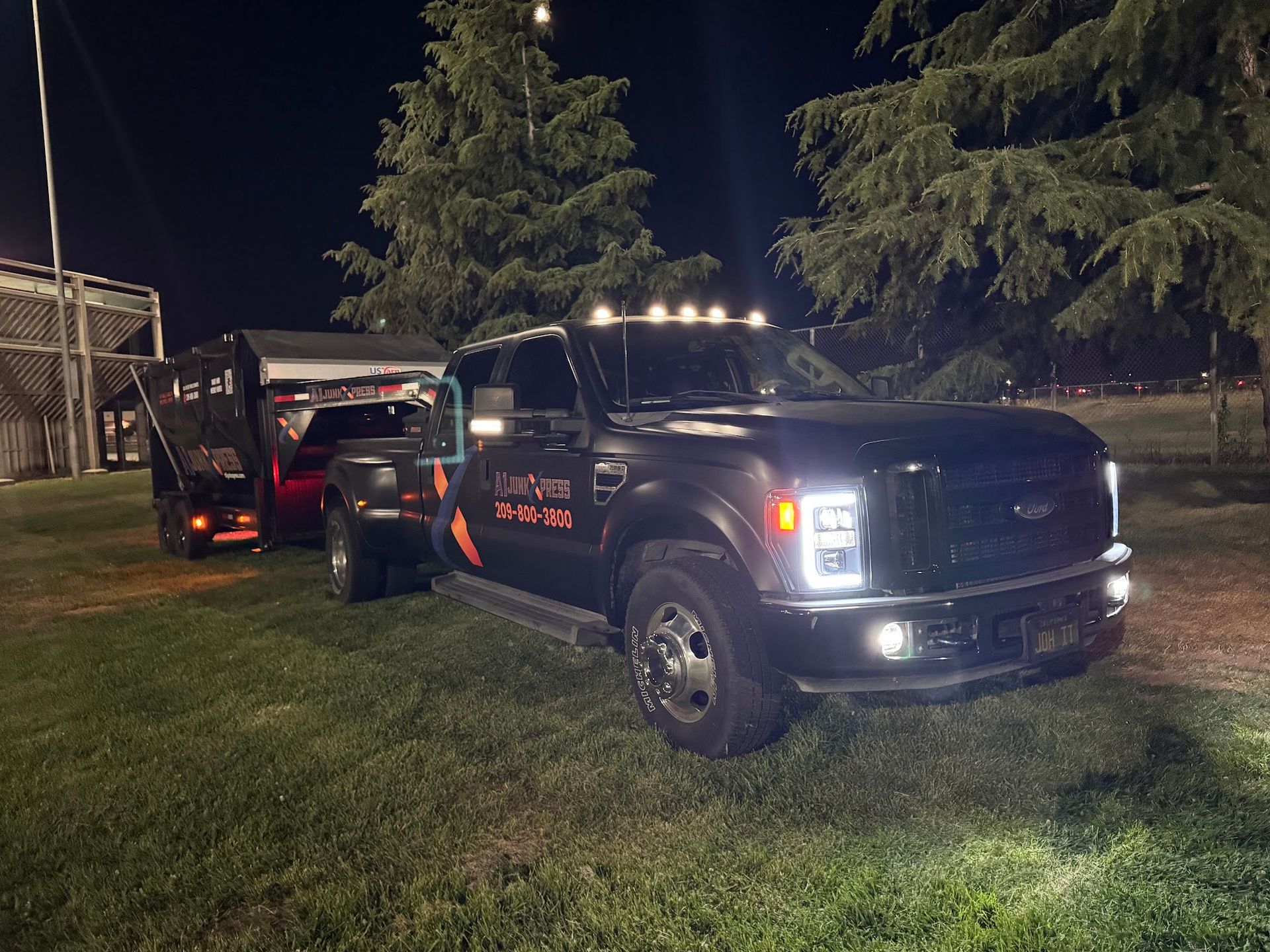 Black tow truck with flashing lights towing a red vehicle at night on a grassy roadside