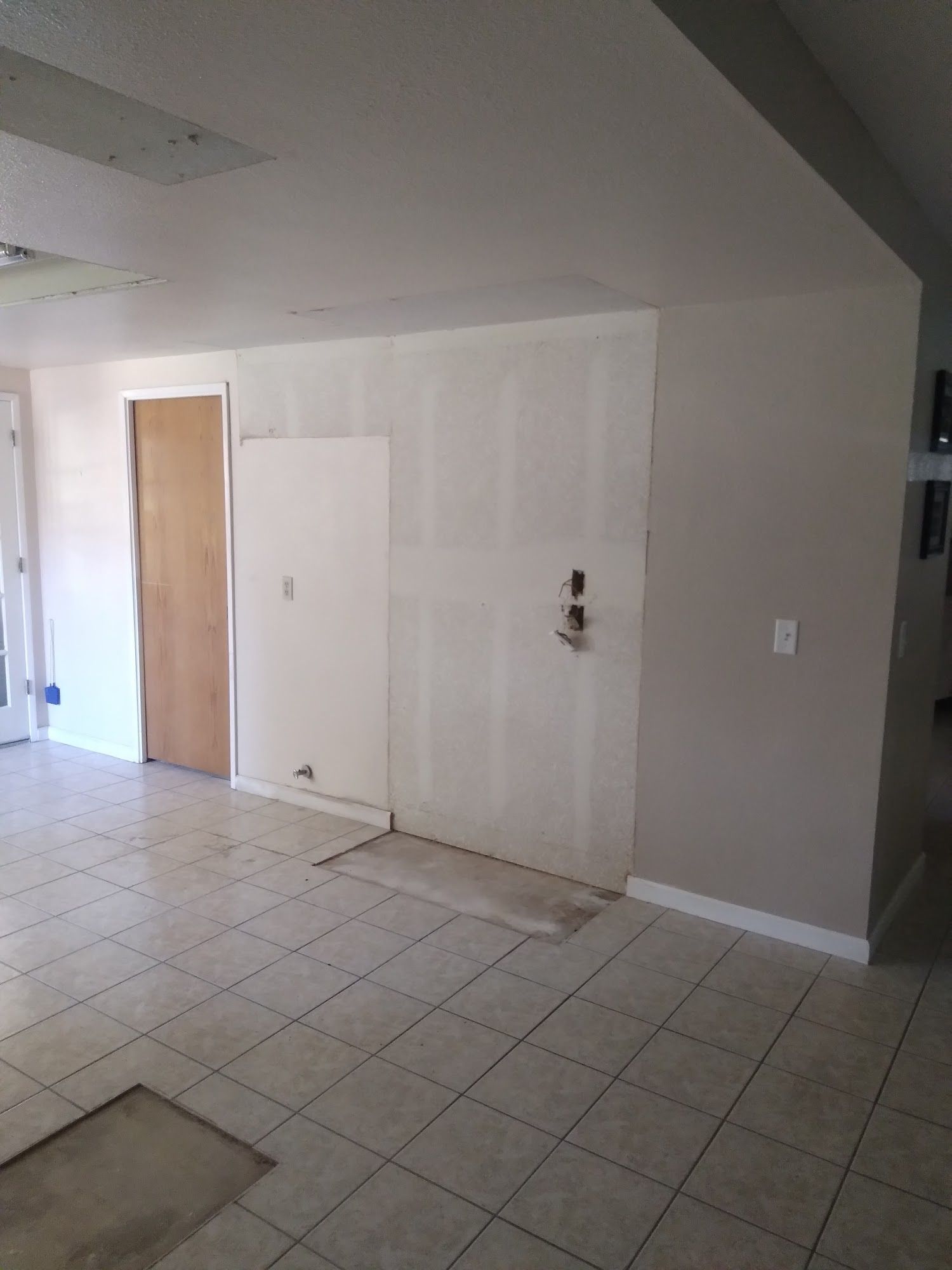 Empty tiled interior room with white walls, a wooden door, and a stairway on the left.