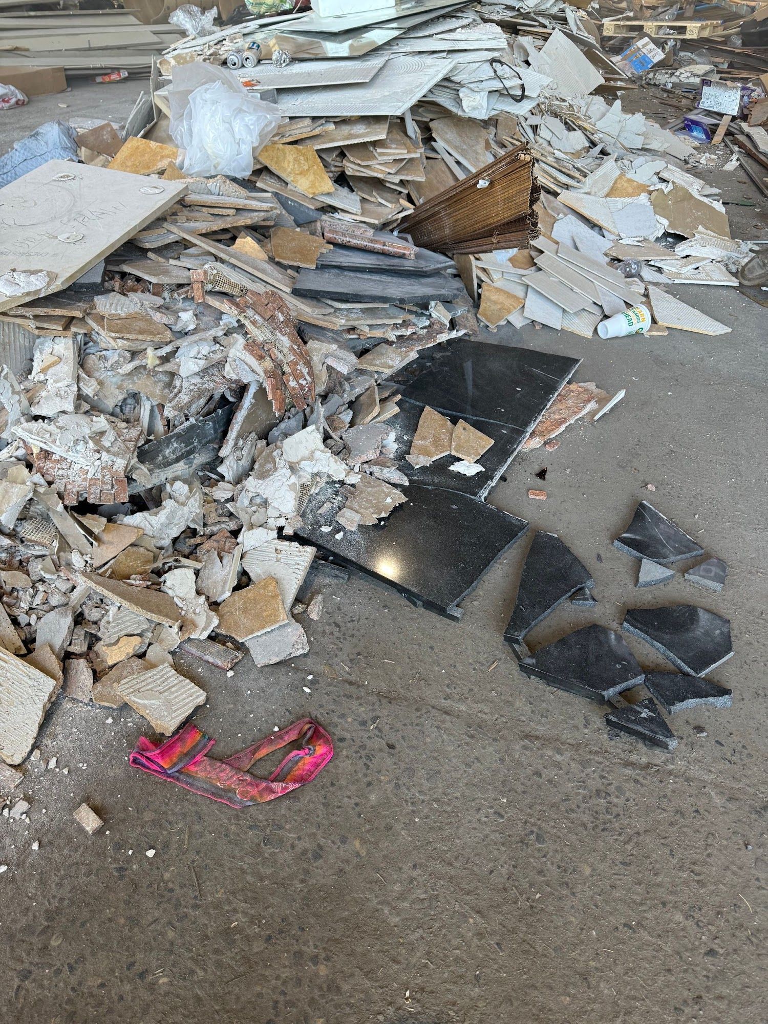 Pile of construction debris and broken tiles scattered on pavement, with black shards and a red strap.