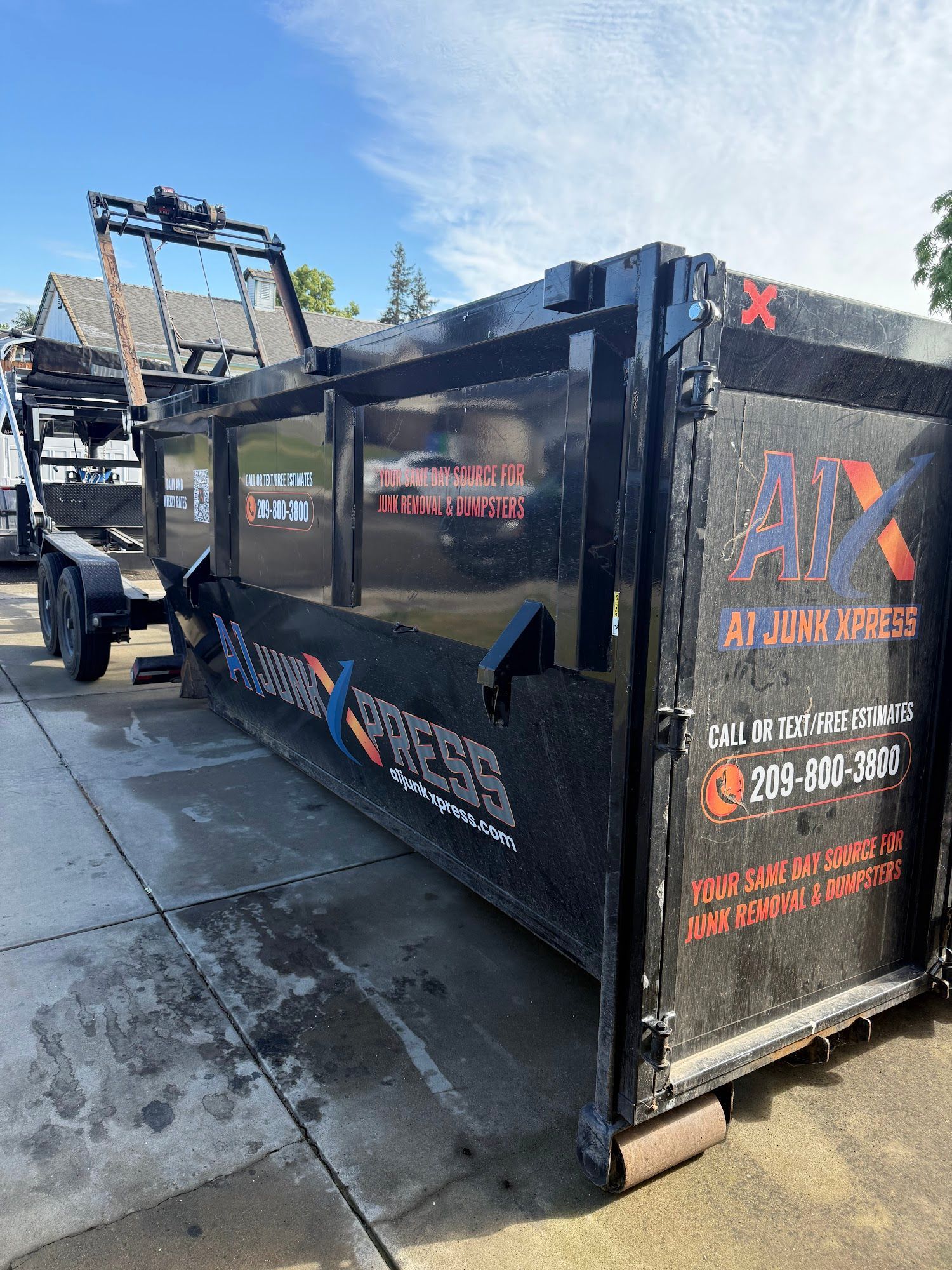 Black construction dumpster on a truck in a sunny parking lot, with an A1 logo and blue sky background