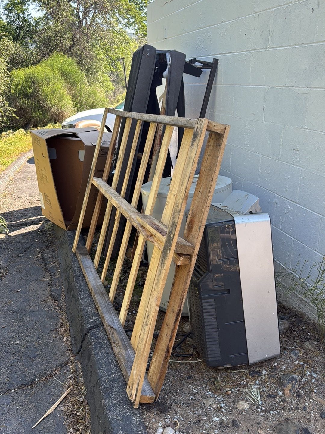 Discarded wooden pallets and furniture piled beside a wall outdoors.