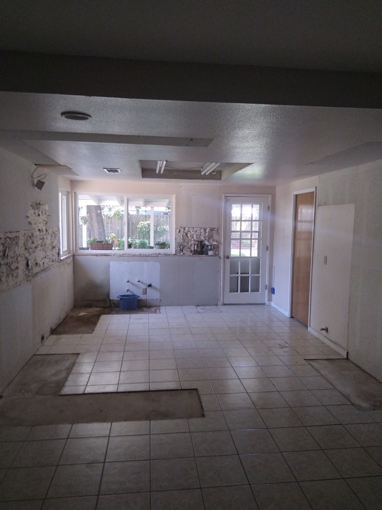 Empty tiled kitchen interior with white cabinets, window, and glass door to outside