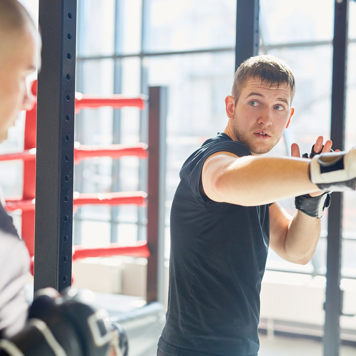 a man wearing boxing gloves looks at another man in a gym