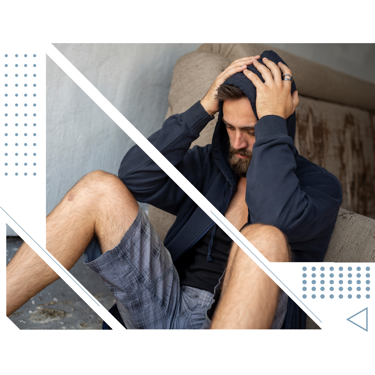 a man in a hoodie sits on a couch with his hands on his head