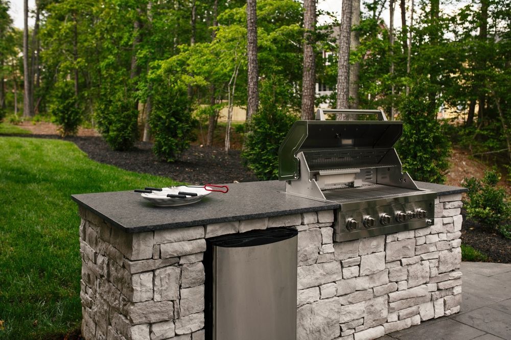 A grill is sitting on top of a stone counter next to a trash can.