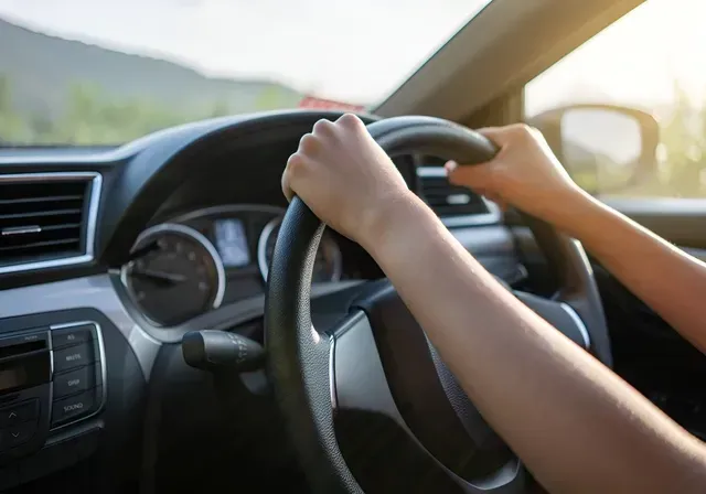 Hands gripping a black steering wheel, driving a car with a dashboard visible.