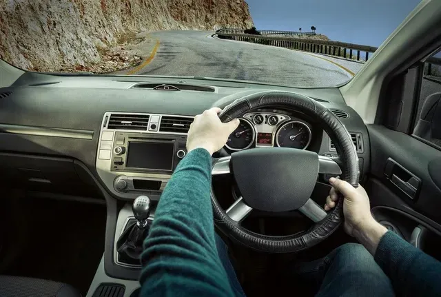 Hands gripping steering wheel driving on a winding coastal road.