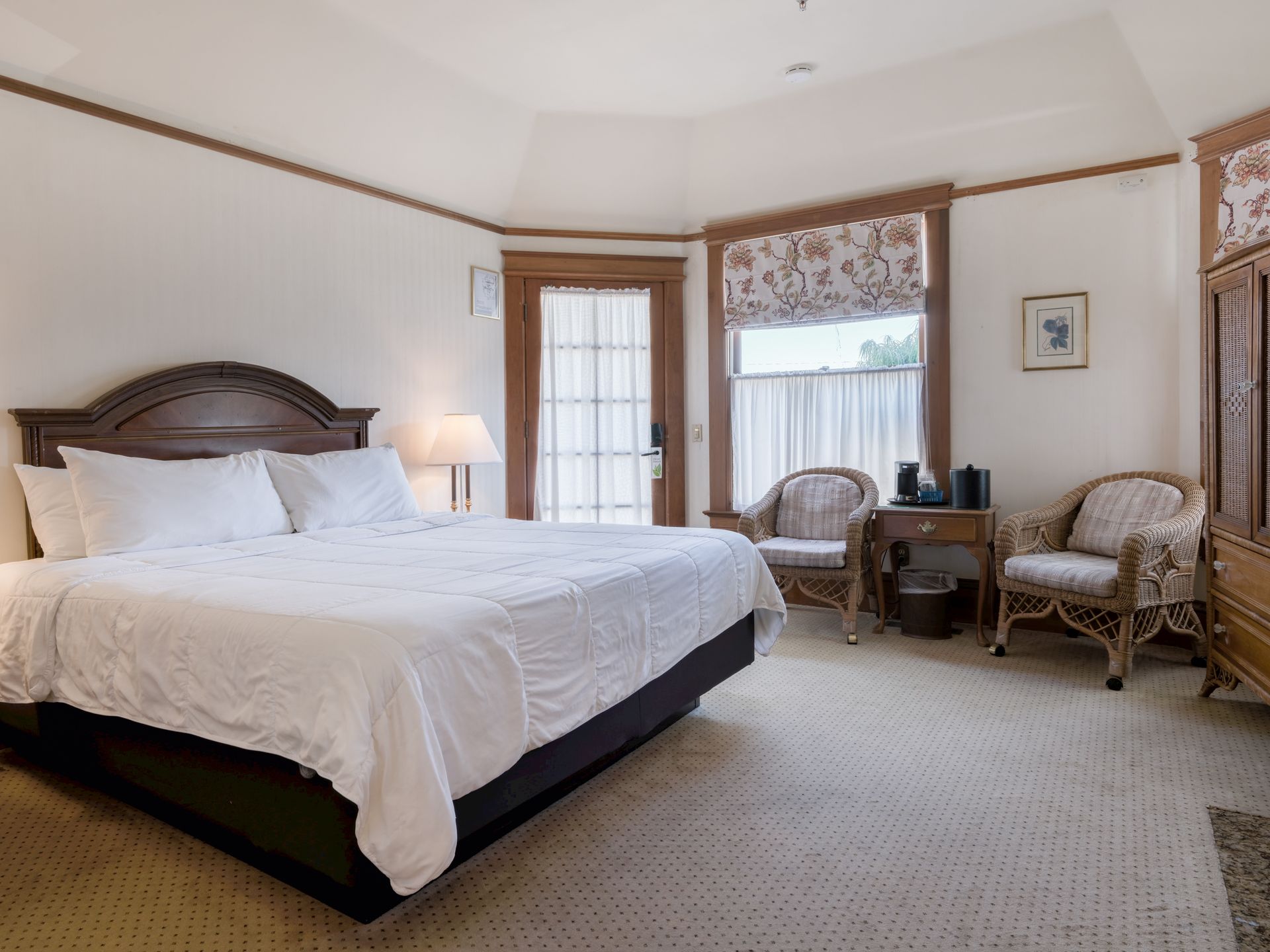 Bright bedroom with a large bed, wicker chairs, and a window with a floral valance.