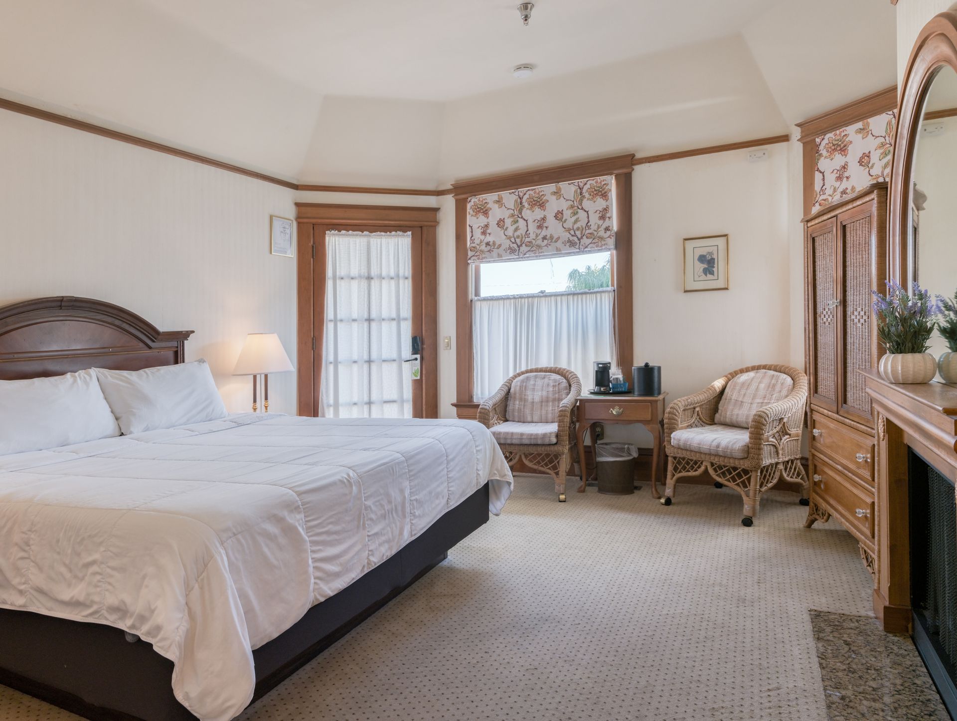 Bright bedroom with a bed, two wicker chairs, large window, and dresser with mirror