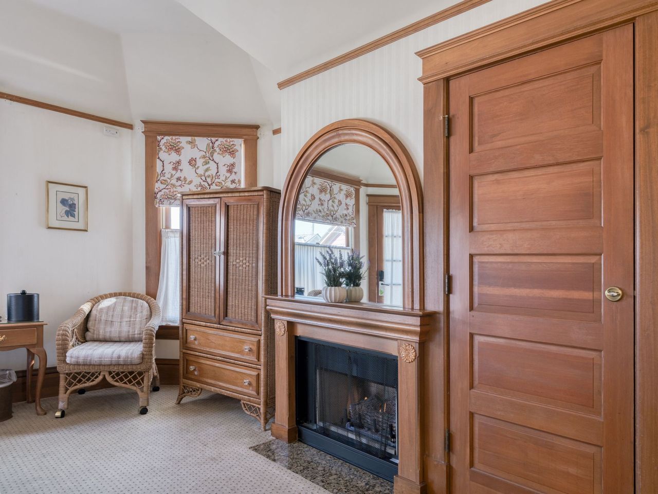 Elegant bedroom with wood furniture, fireplace, arched mirror, and upholstered chair