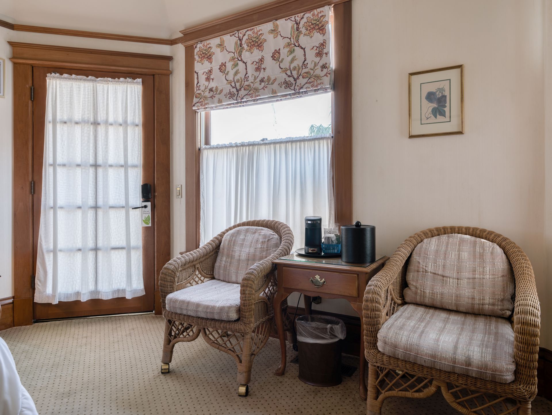 Bright sunroom with two wicker chairs, small table, and wood-framed glass door with curtains.