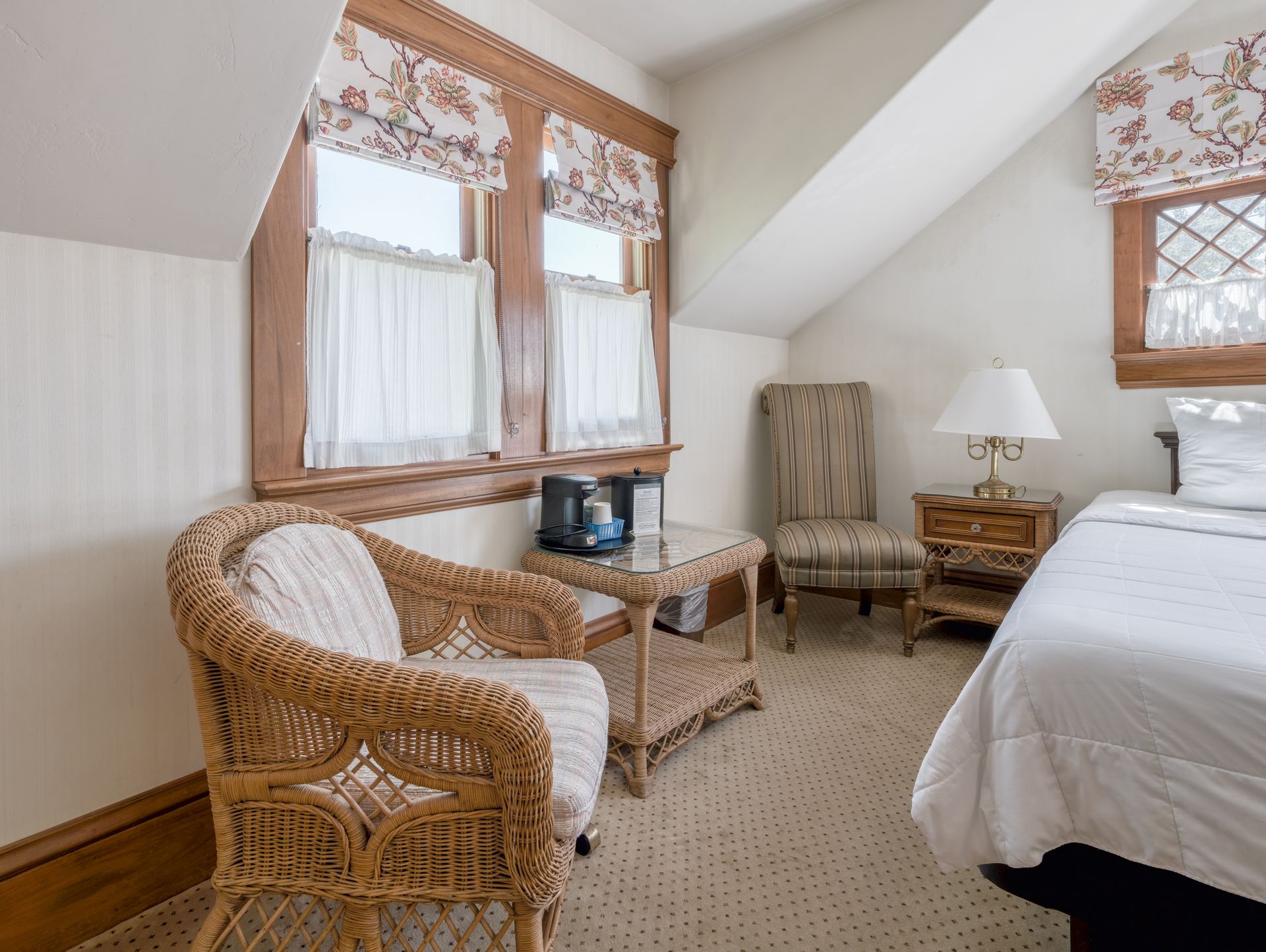 Cozy attic bedroom with wicker chairs, bed, and lace-curtained windows