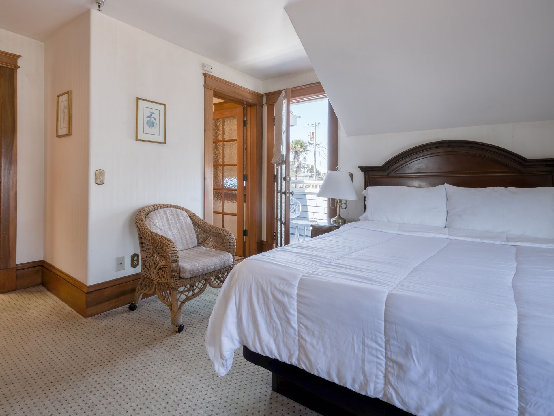 Bright bedroom with a large bed, wicker chair, and open door to a sunlit balcony.