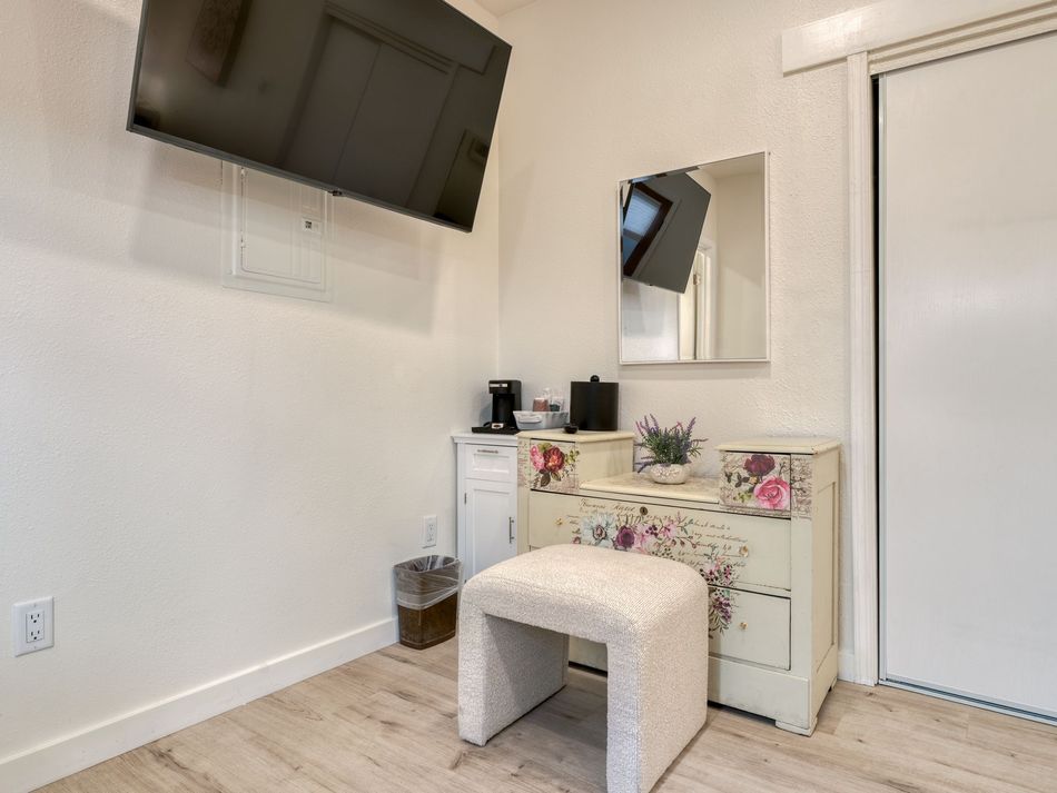 Bedroom vanity with wall-mounted TV, mirror, white dresser, and pink cushioned stool