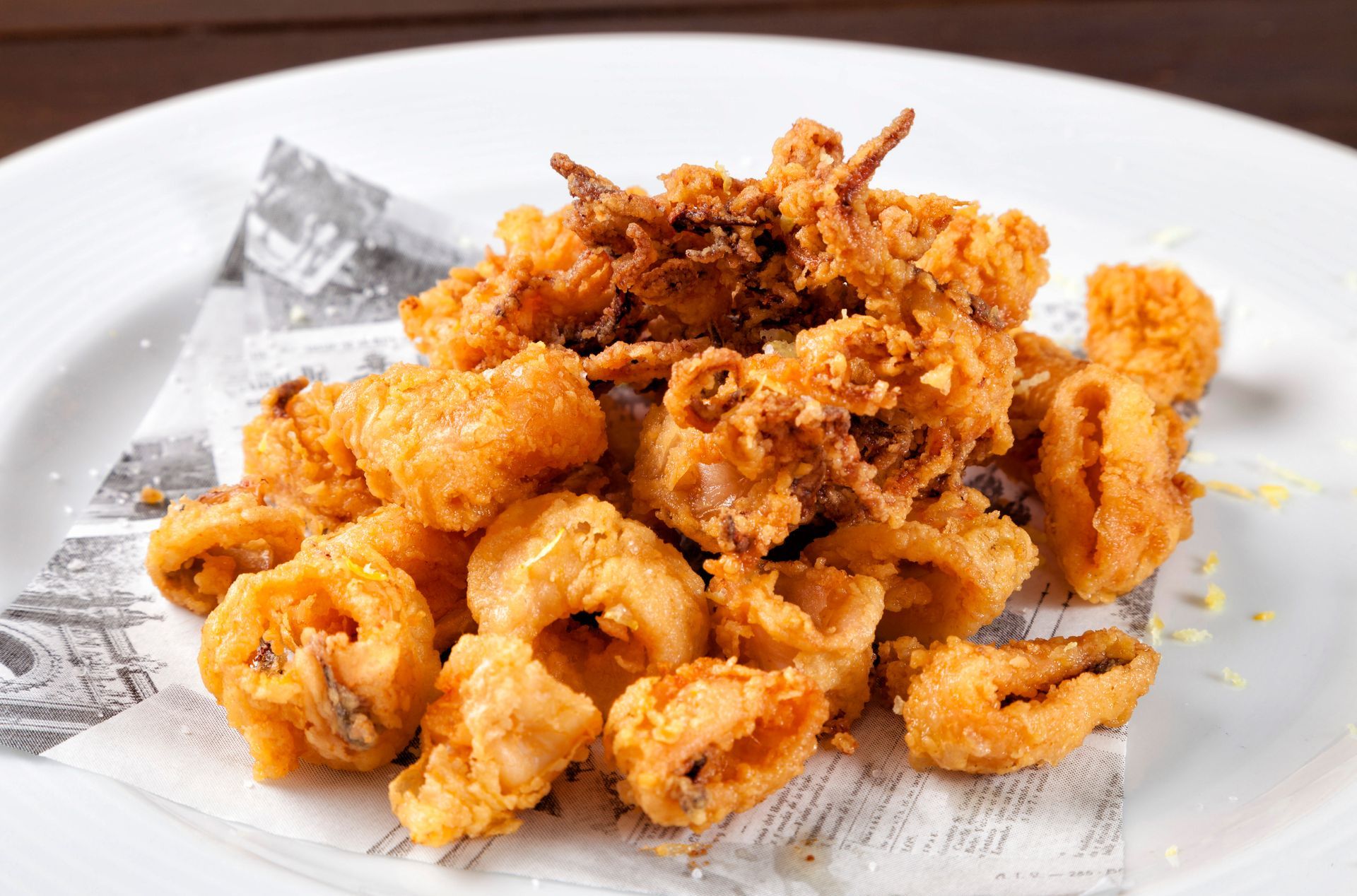 Plate of golden fried calamari topped with crispy onions on white parchment-lined dish