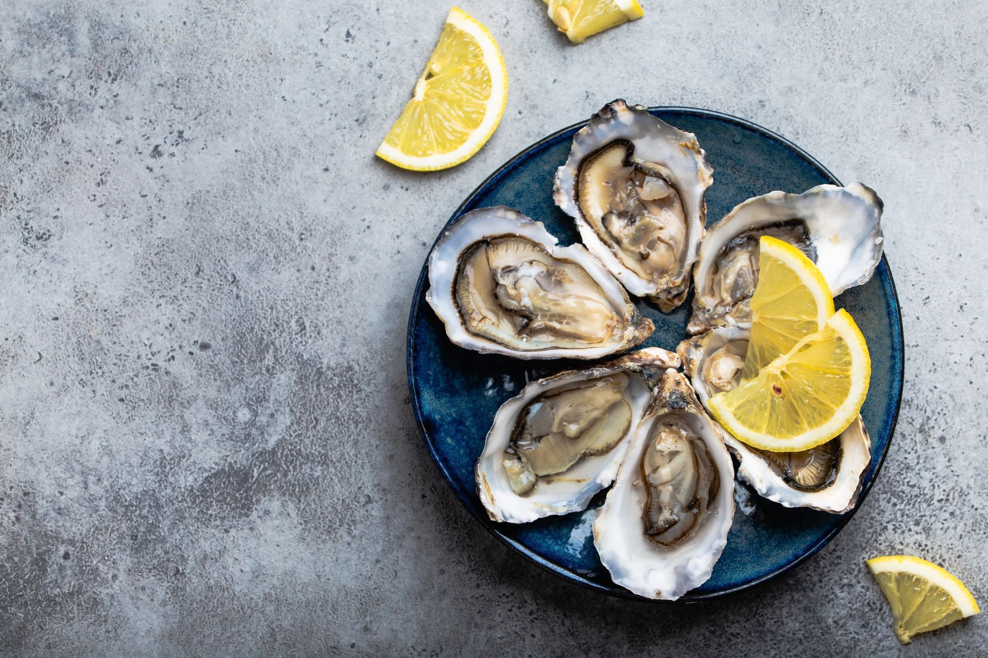 Oysters on a blue plate with lemon wedges on a gray surface
