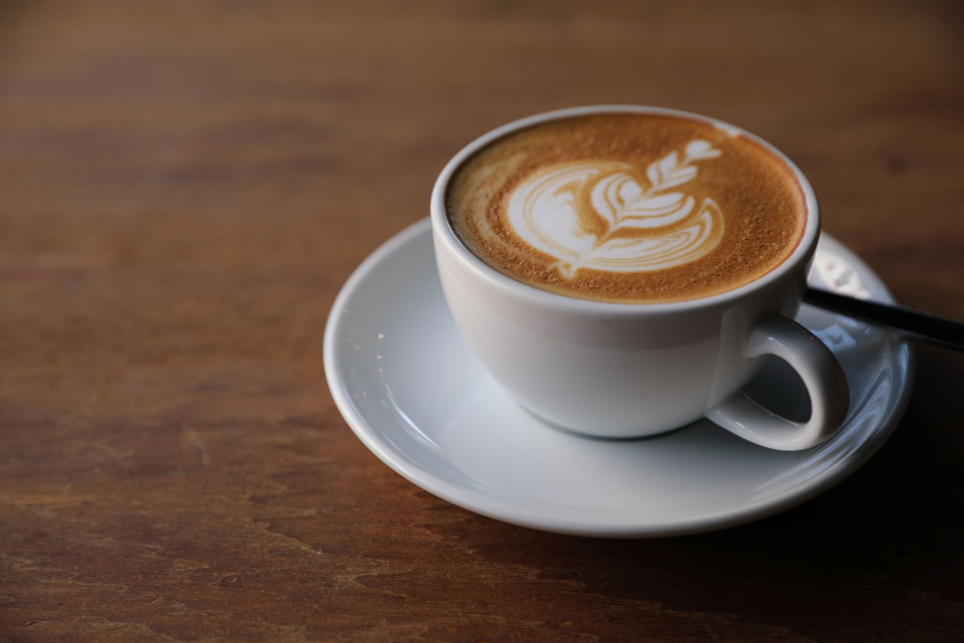White cup of latte with leaf latte art on a saucer on a wooden table