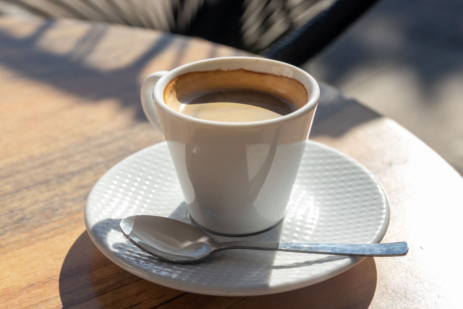 White cup of coffee on a saucer with a spoon, on a sunlit outdoor table