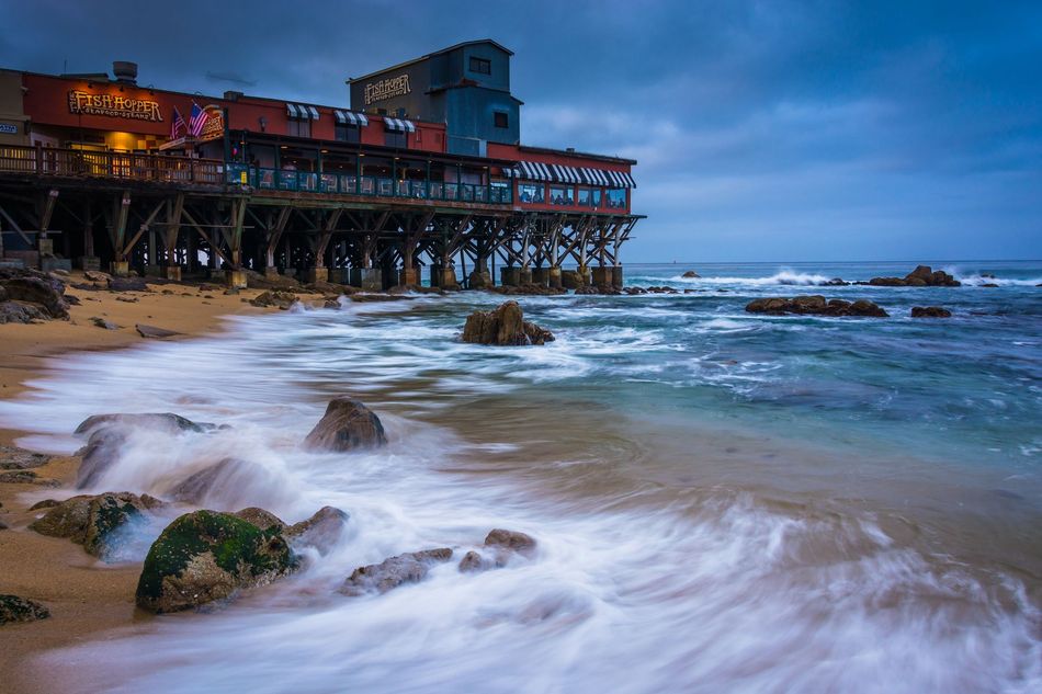 Rough surf washing over a sandy beach beside a stilted seaside building at dusk