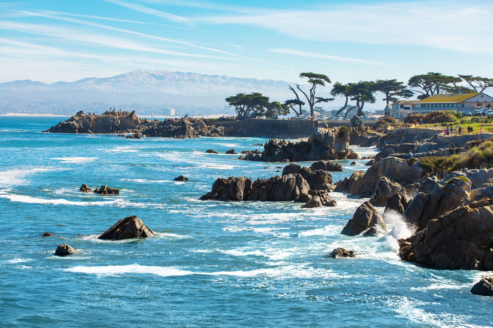 Rocky coastline with turquoise waves, sea cliffs, and trees under a clear blue sky