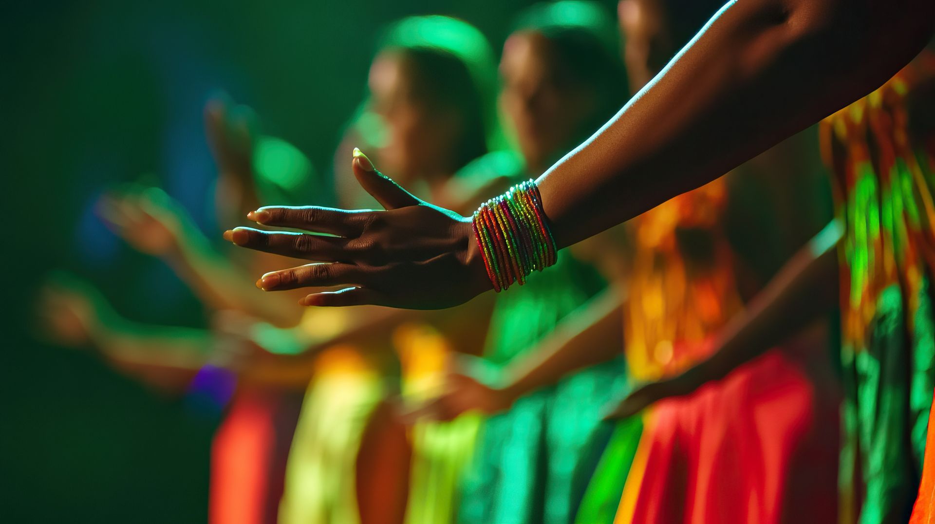 Dancers in colorful dresses with raised hands performing on a stage under green and orange lights