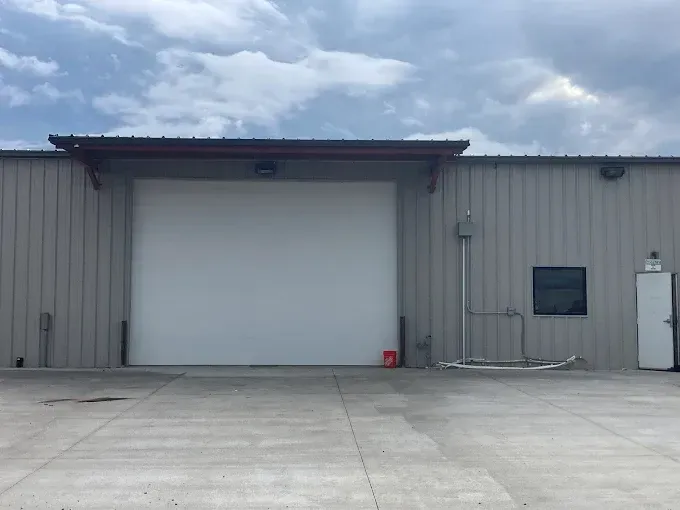 Industrial warehouse exterior with a large white loading door and gray metal siding under a cloudy sky