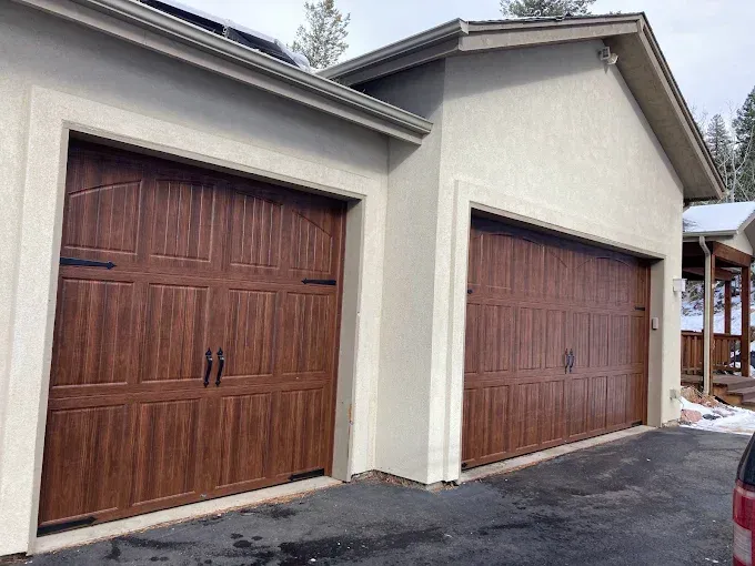 Two wooden garage doors on a beige house exterior, one double and one single.