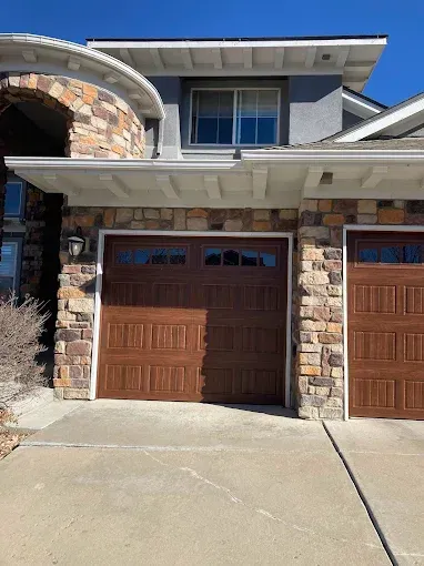 Suburban house exterior with stone facade, brown garage doors, and concrete driveway
