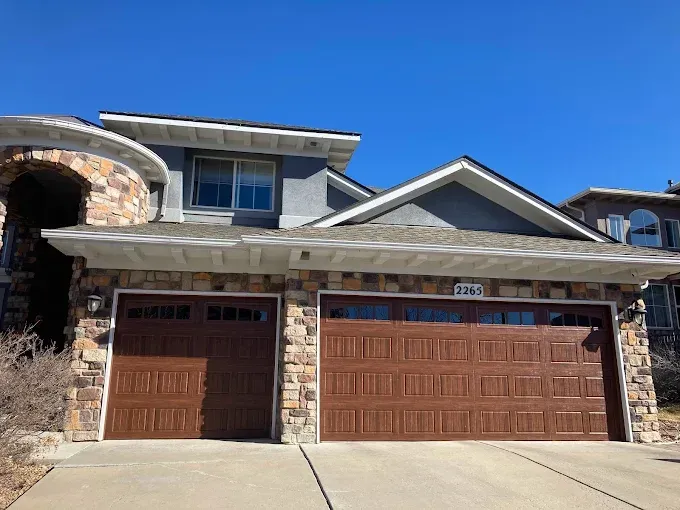 Suburban stone house with a brown three-car garage and blue sky above