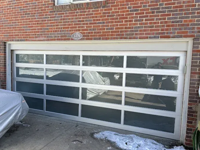 Brick garage with a frosted glass overhead door and snow on the driveway