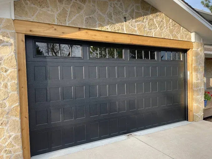 Black paneled garage door beneath a stone archway on a house exterior