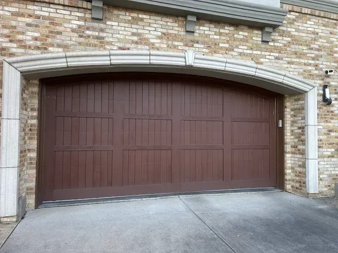 Brown double garage door set in a brick house facade with a concrete driveway.