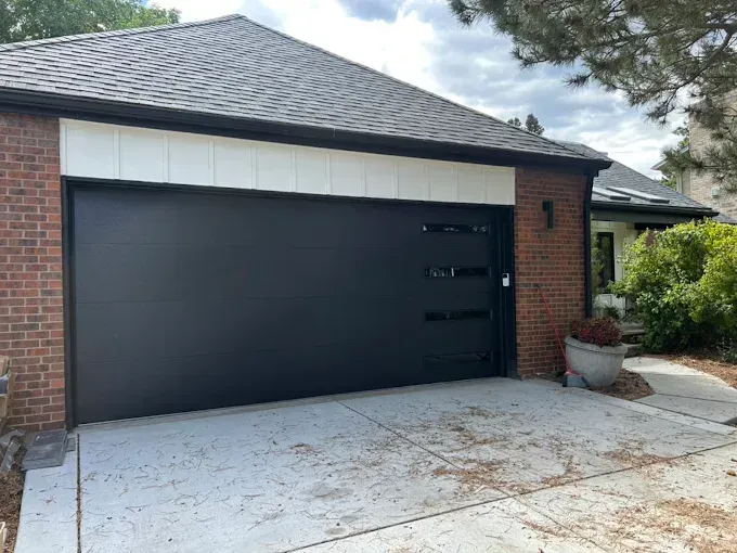 Detached brick house with a black garage door and light concrete driveway