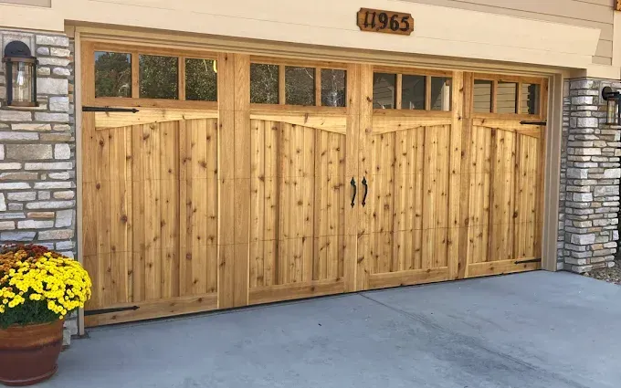 Wooden garage doors on a house, framed by stone columns and a potted yellow flower arrangement.