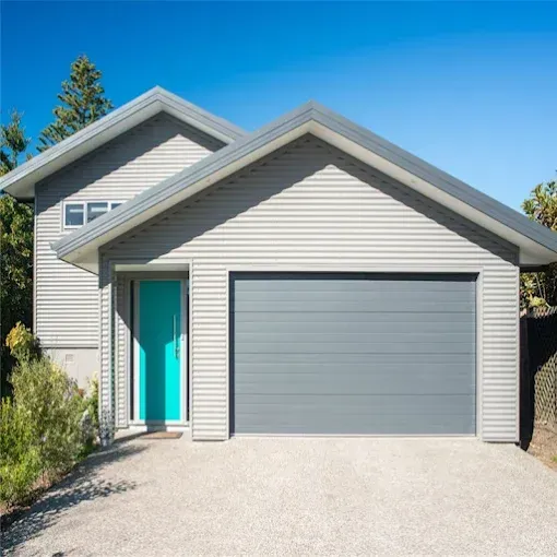 Modern house exterior with gray siding, turquoise front door, and a two-car garage under a blue sky
