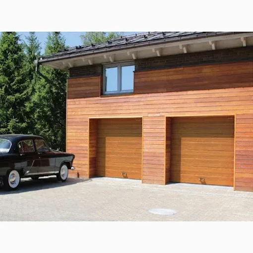 Modern wooden garage with two orange doors and a vintage black car parked outside under a clear sky