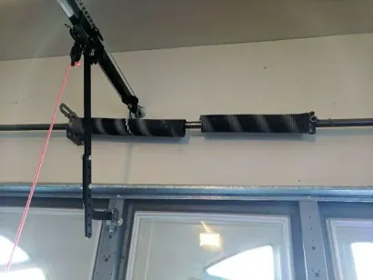 Garage door opener mounted above a glass door, with black hardware and a pink cord.