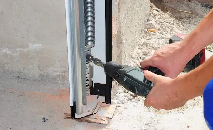 Hand drilling a metal bracket into a wall beside a vertical threaded rod