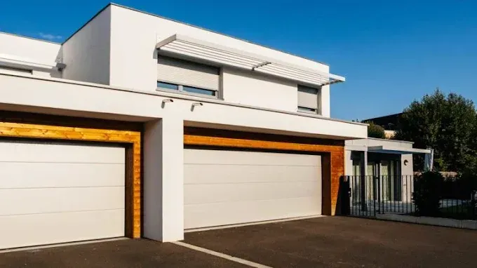 Modern white house with two garage doors and a driveway under a clear blue sky