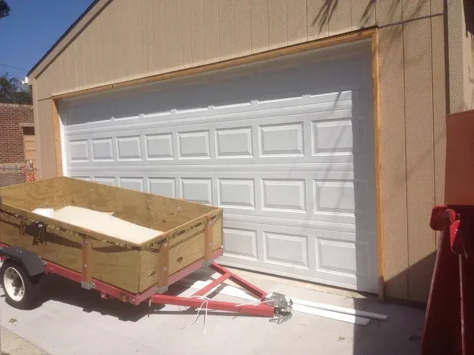 Small trailer loaded with a wooden crate parked in front of a white garage door.