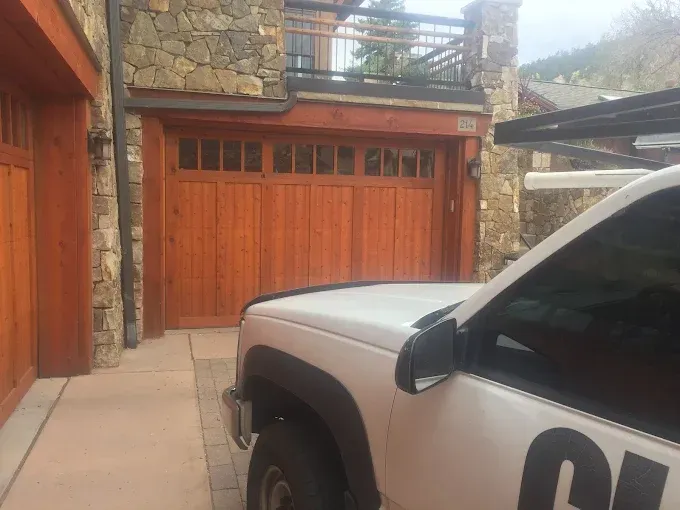 White SUV parked beside a wooden garage and stone house driveway