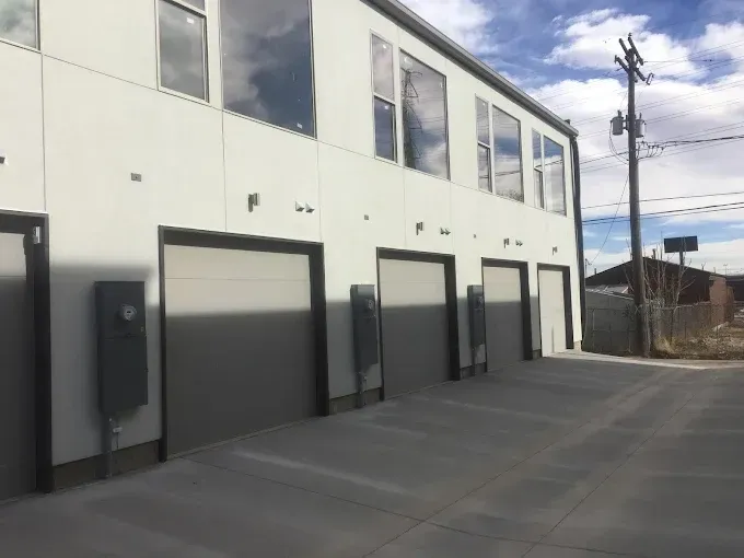 Row of gray garage doors on a white industrial building beside a paved driveway under a cloudy sky