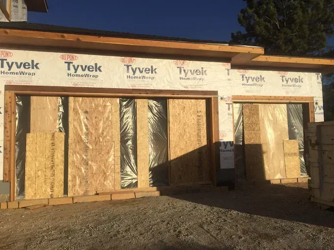 Framed house under construction with Tyvek wrap, plywood panels, and open door and window frames