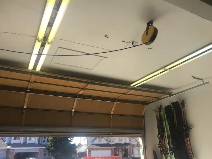 Open garage door with overhead lights and stored tools along the wall
