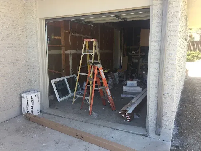 Open garage under renovation with ladders, boards, and construction materials inside.